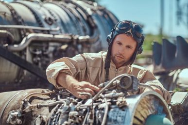 portrait-pilot-mechanic-uniform-flying-helmet-repairing-dismantled-airplane-turbine-open-air-museum